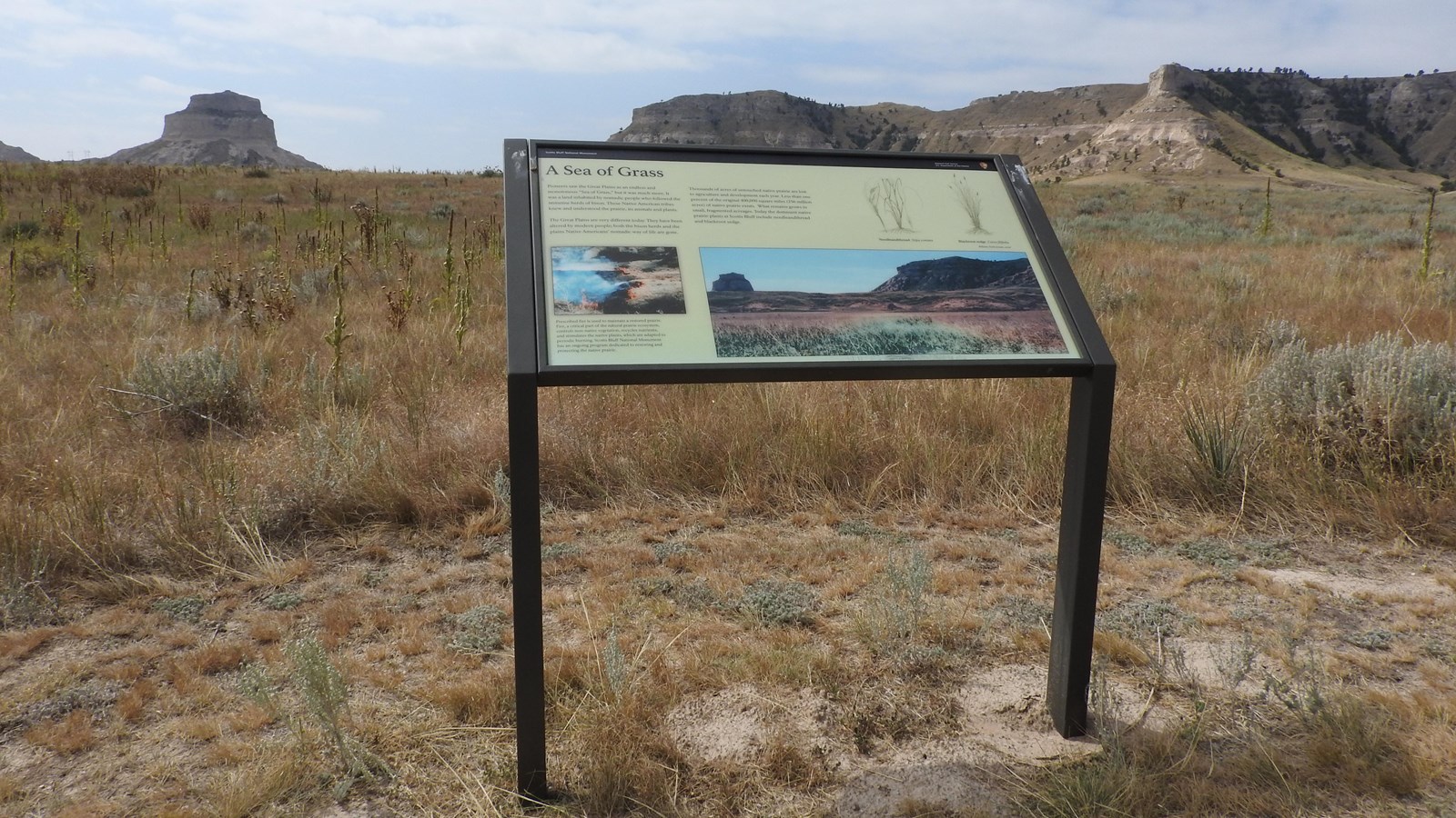A wayside panel overlooks the prairie and distant sandstone bluffs. 