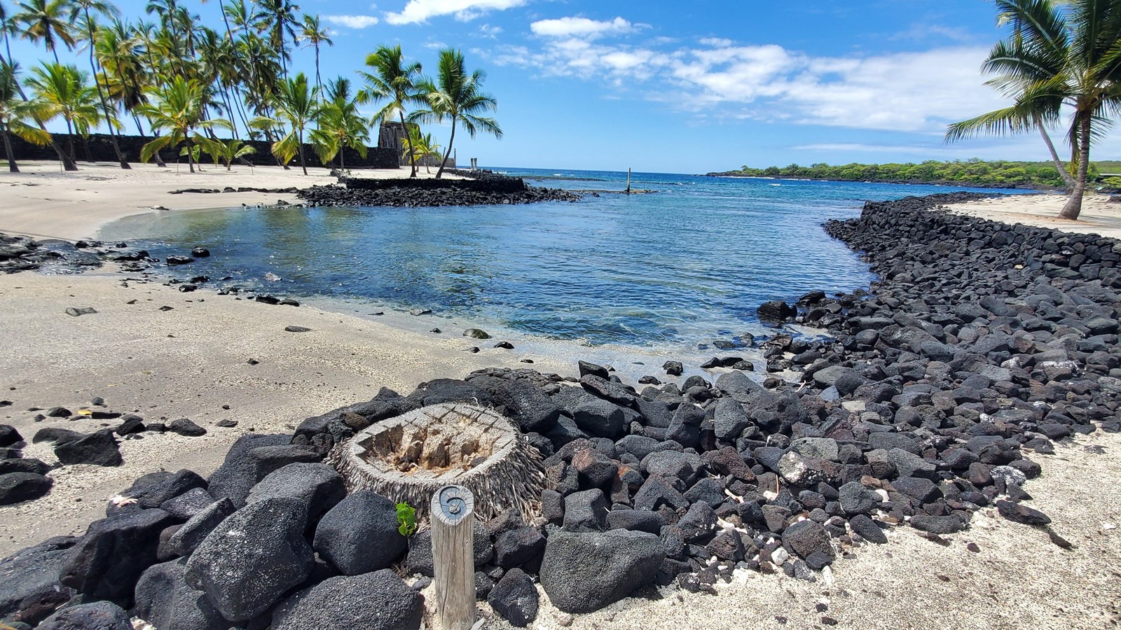 A protected cove with lava rock sea walls on two sides and a sandy beach area.