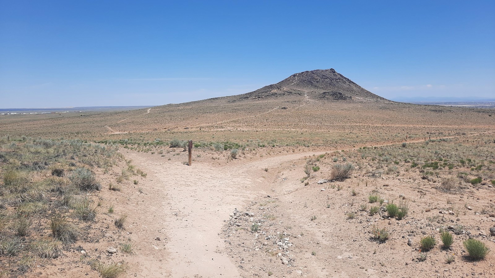 A dirt trail through an arid landscape with a volcano in the distance.