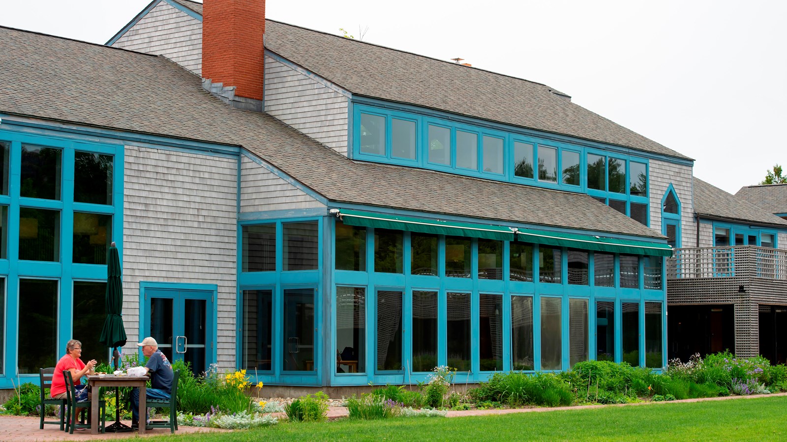 A two story grey building lined with windows and blue trim in front of a green lawn