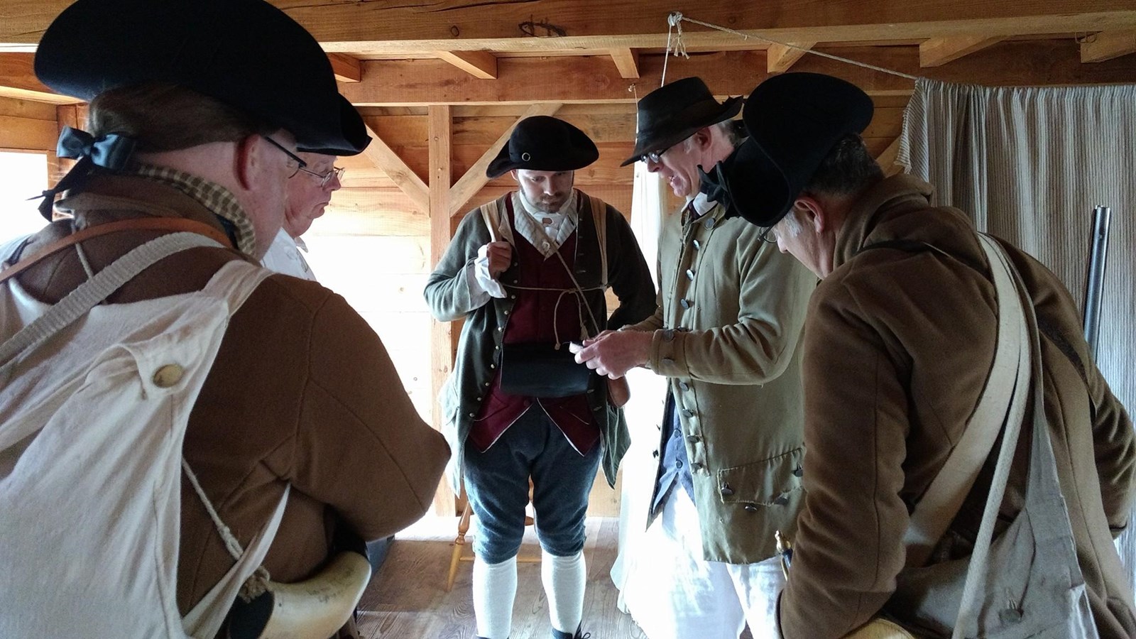 Several Continental soldiers gather at the center of the room to have a conversation.
