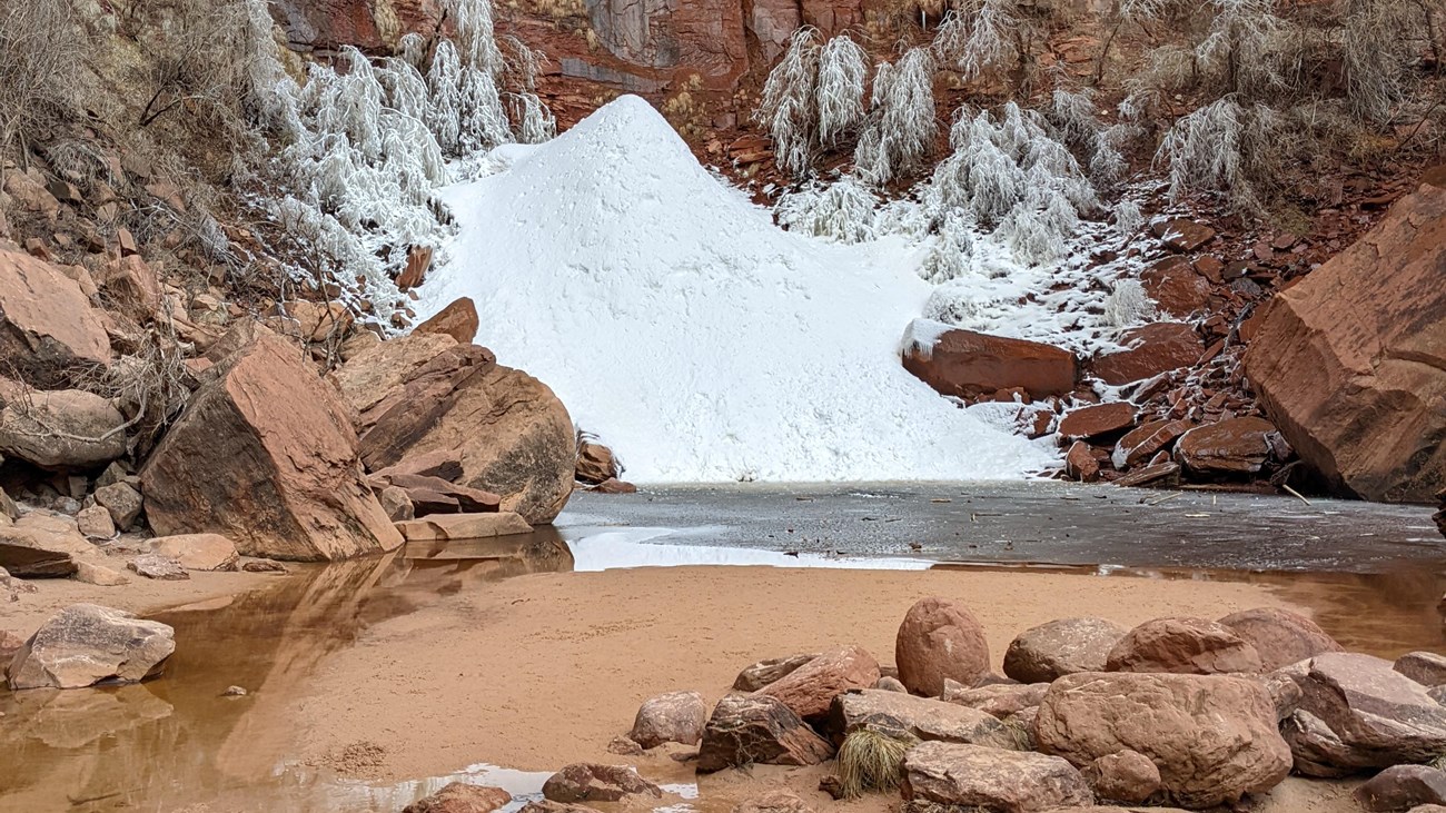 A mound of ice and snow surrounded by red sandstone rocks.