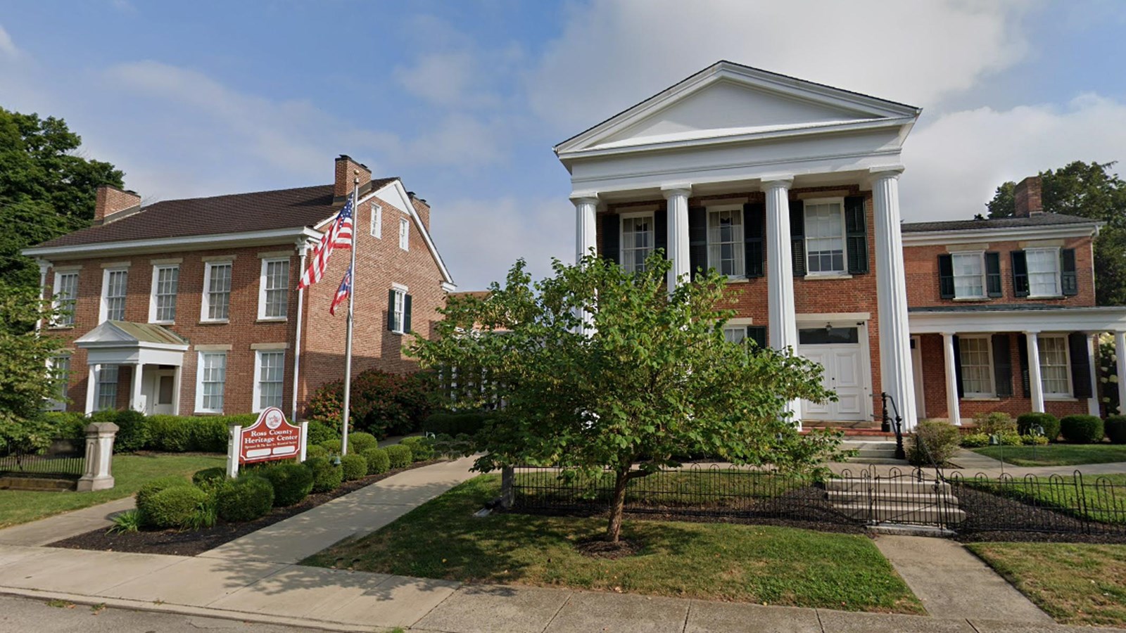 A large building with four tall columns holding up a peaked roof next to a brick two-story house