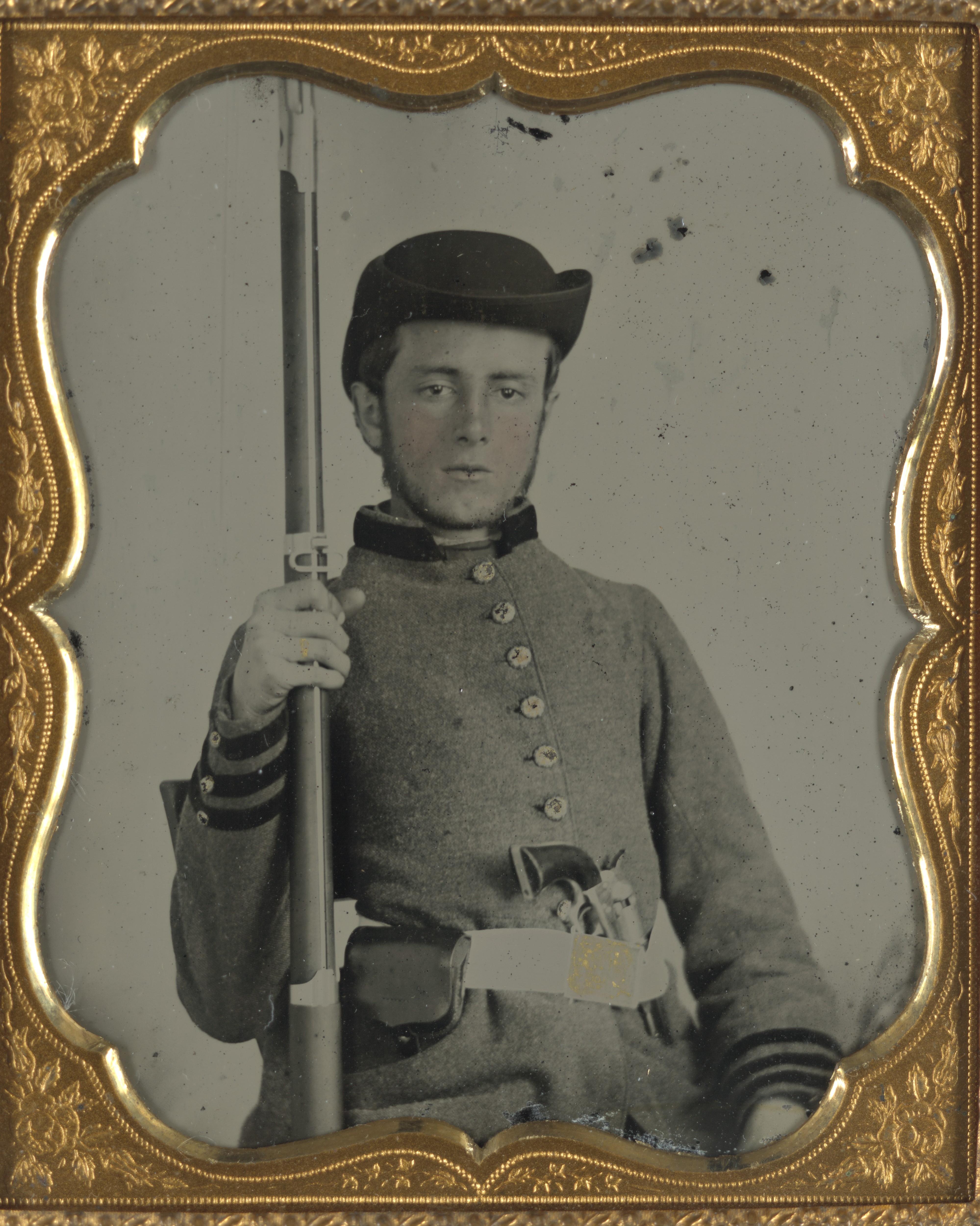 A Civil War portrait photo shows a young soldier posing in a Confederate uniform with his musket. 