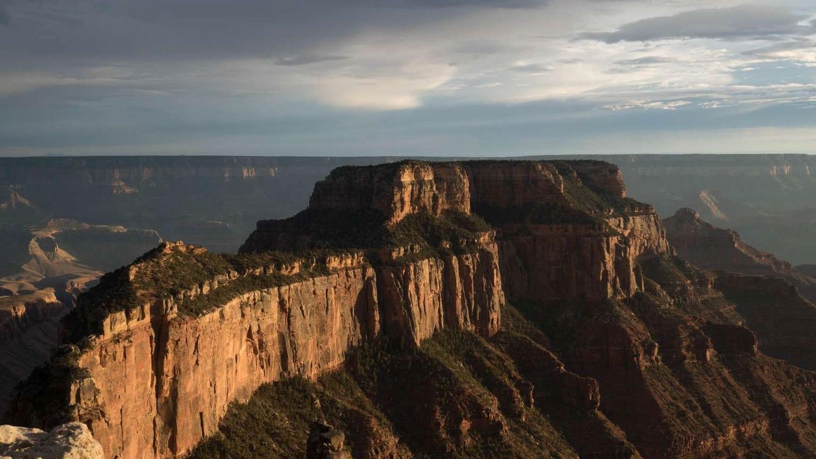 A fin of rock extends into the distant canyon, sunset bathes the rocks in golden light