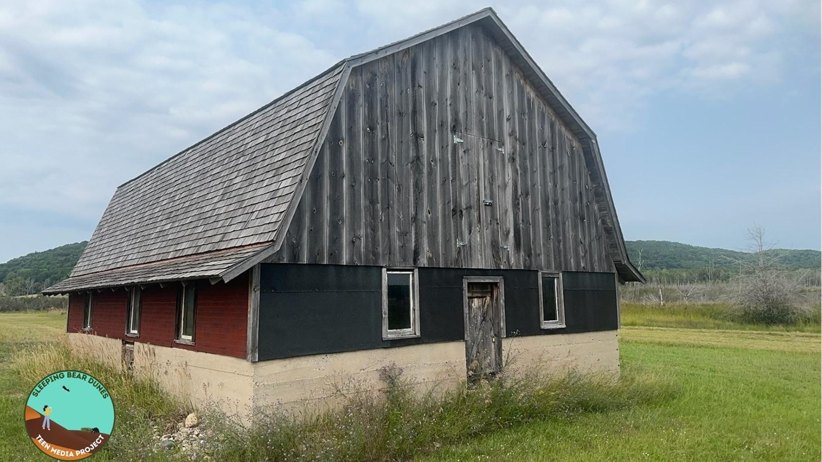 Sitting in a field by itself, a barn with a cedar roof with one red side and one green side.
