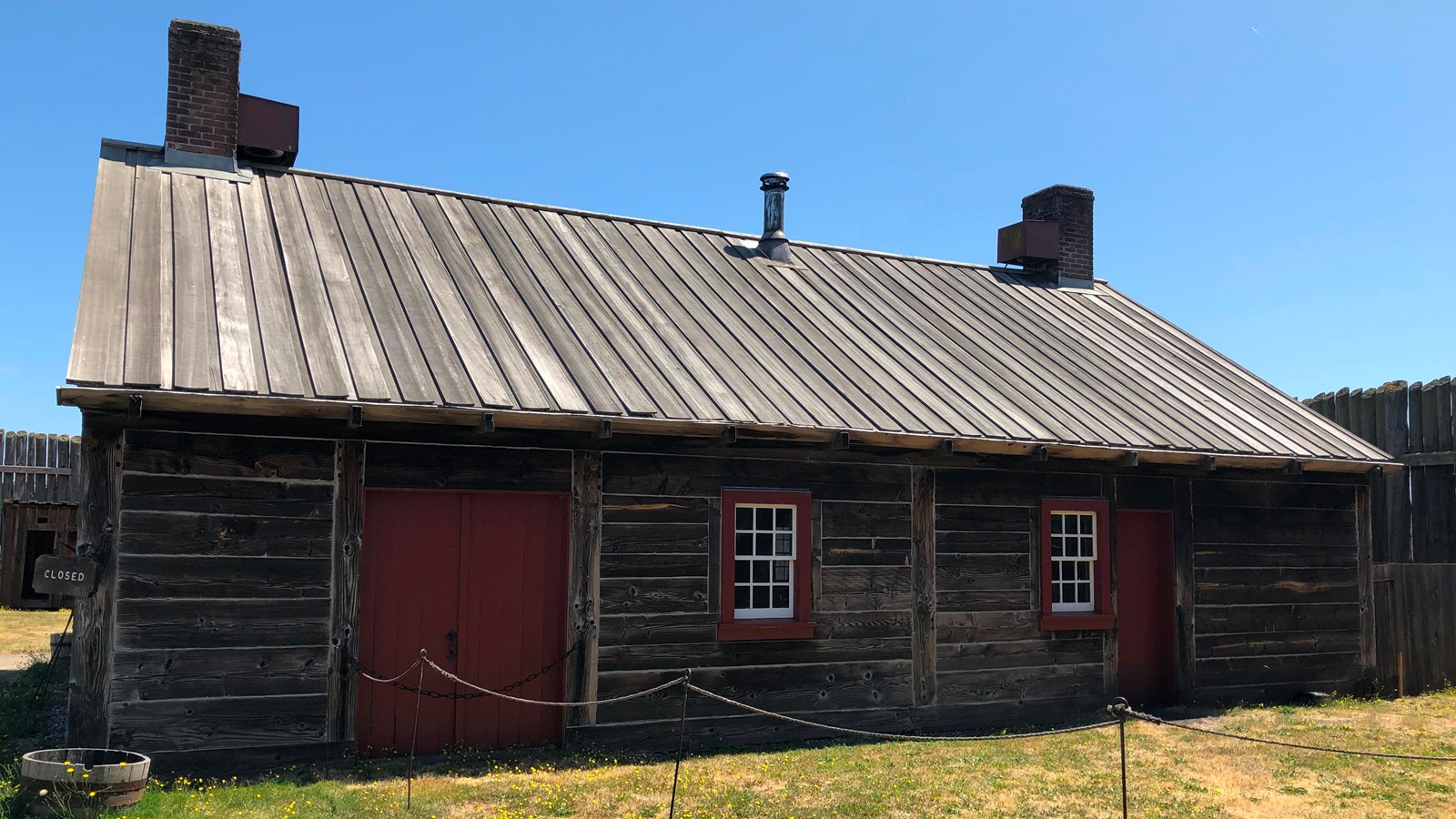 A rectangular building with two chimneys, windows, and a double-door entrance.