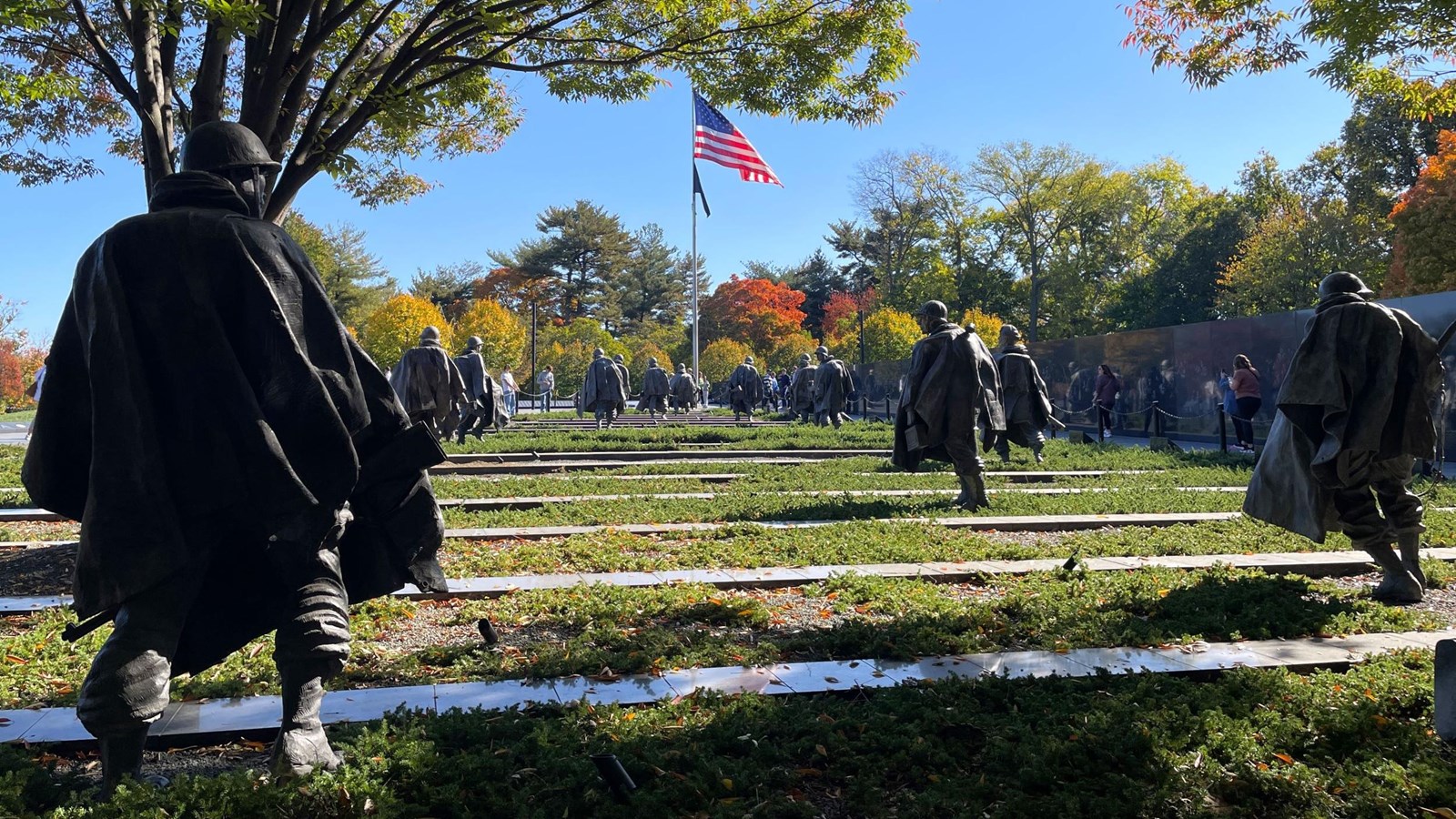 Several bronze statues of soldiers in a field with the American flag in the distance