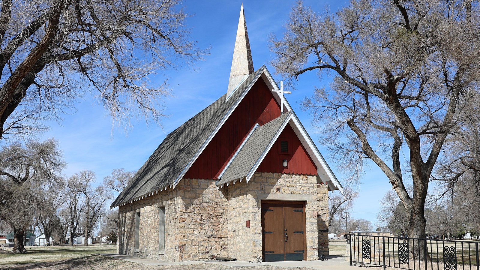 A small gray stone and red church building with a pointed roof and a steeple.