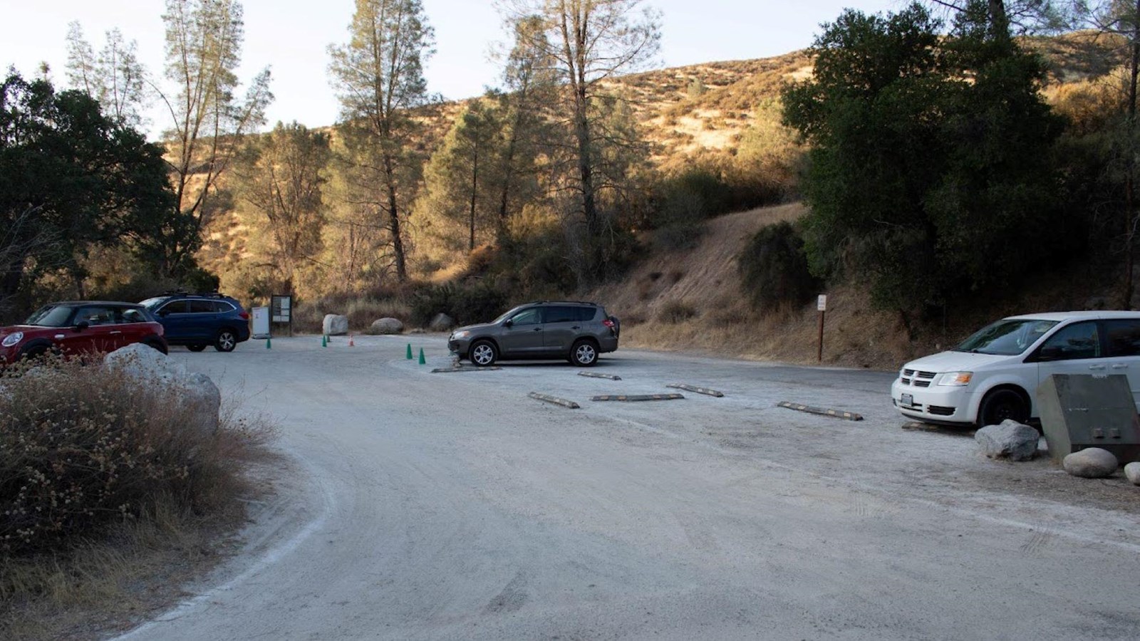 Gravel parking area situated next to a hillside blanketed with shrubs, blue oak, and grey pine trees