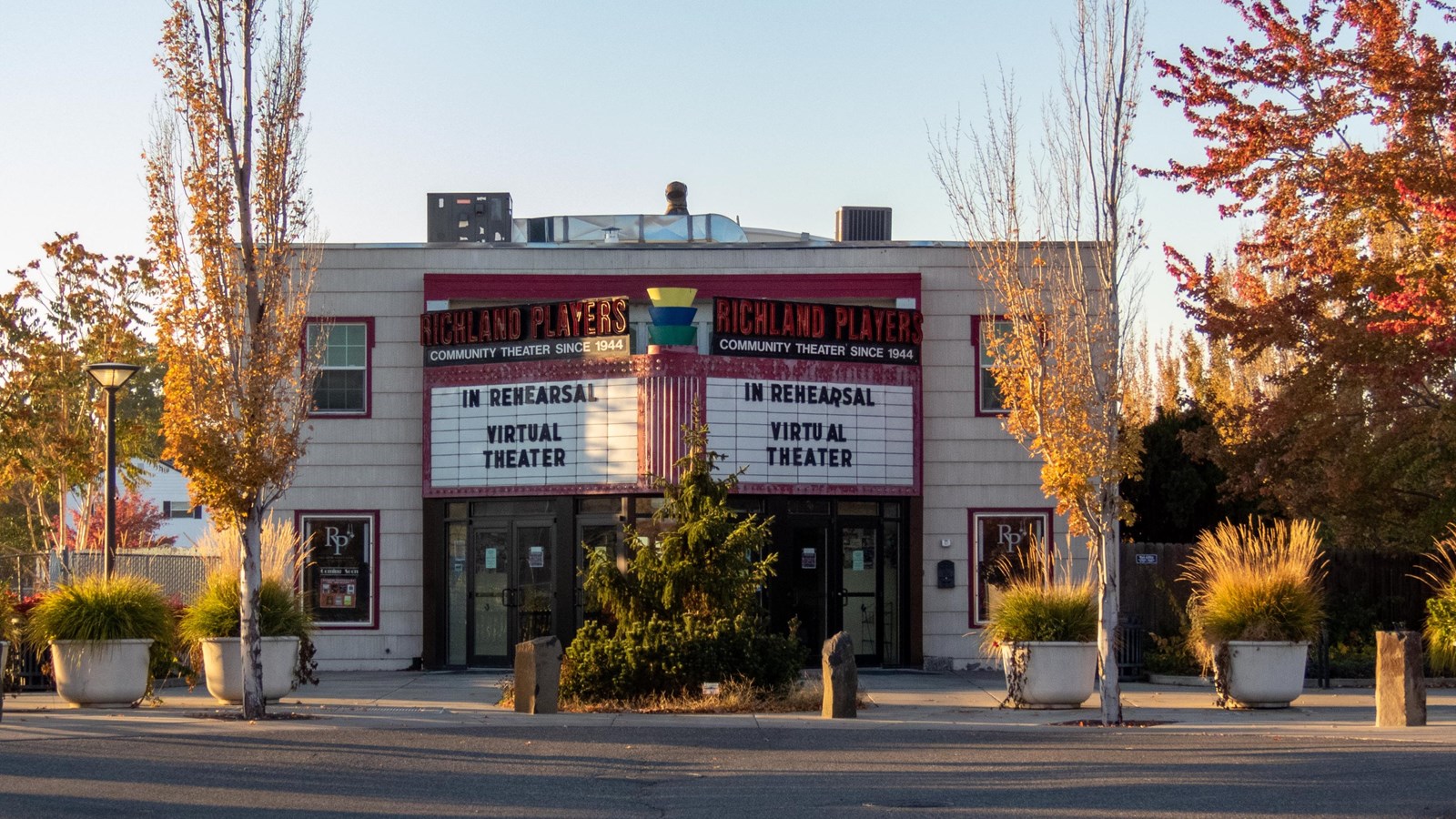 A wood building with a large marquee trees with fall red leaves are alongside the building