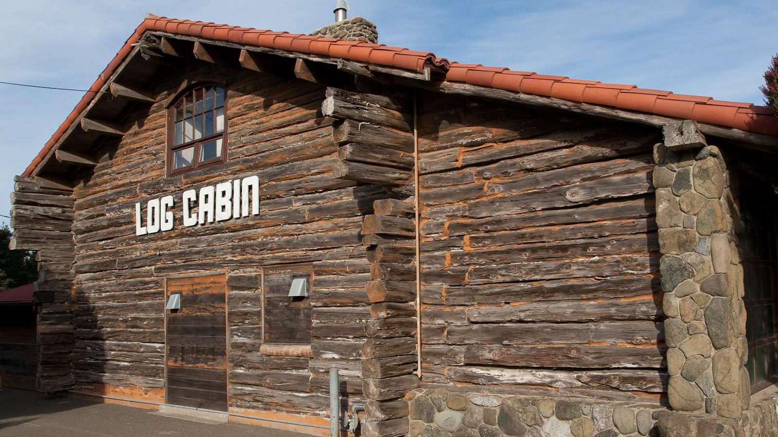 The log cabin from the front showing the stacked logs and natural stonework.