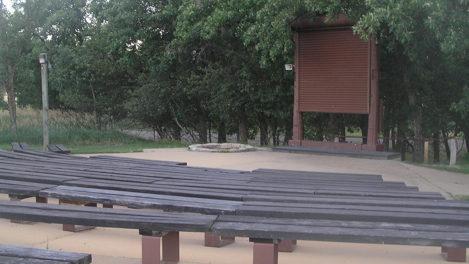 rows of curved benches around a flat stage area with screen and fire pit