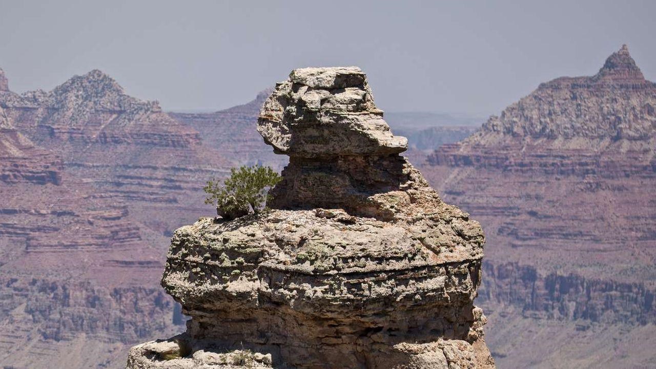 A piece of rock extending above the canyon rim roughly shaped by erosion in front of distant rocks