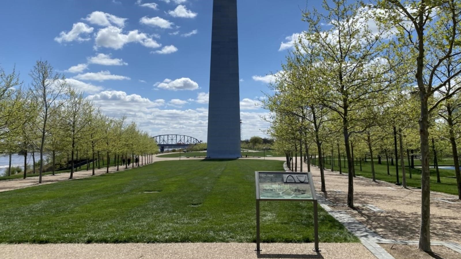 looking at the north leg of the Arch behind a green lawn with a sign with exhibit text on it