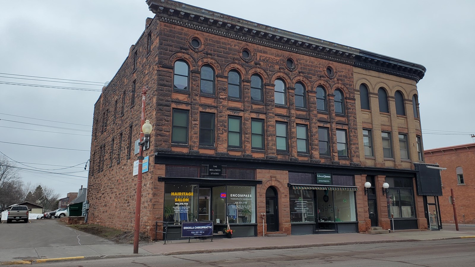 Three story red sandstone block building with decorative roof trim.