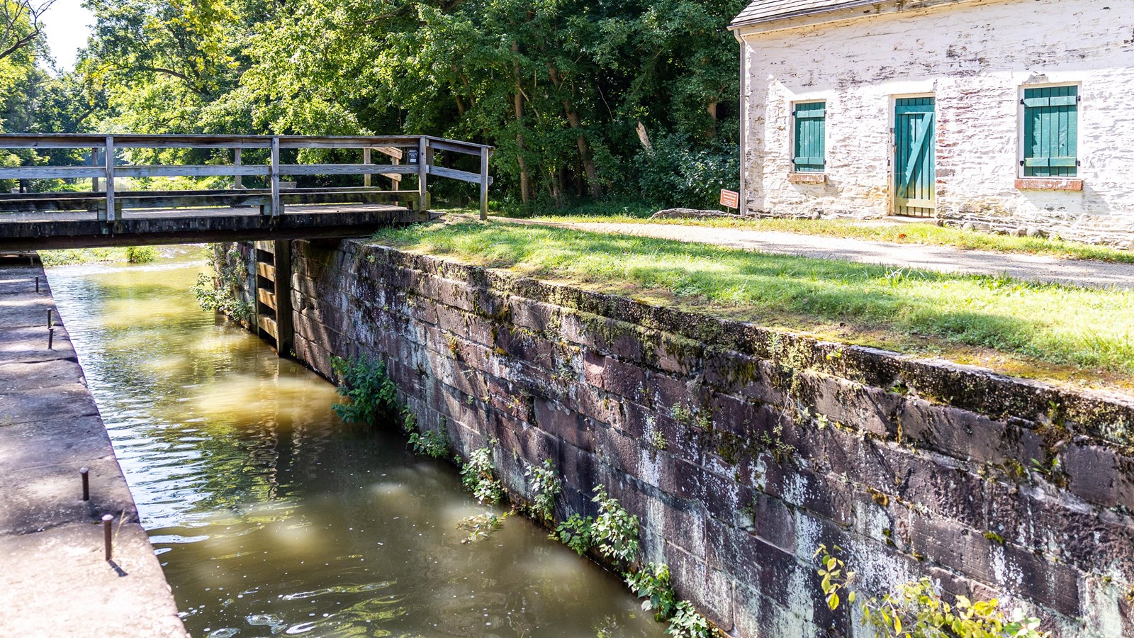 A wooden bridge across a watered lock with historic lockhouse