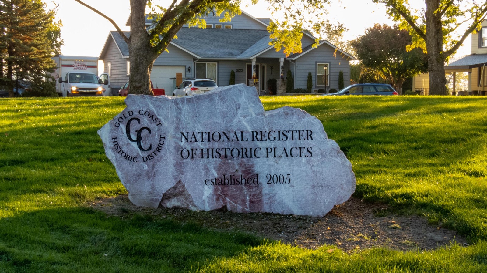 Color photograph of a rock with writing on it laying on a green lawn in front of suburban homes
