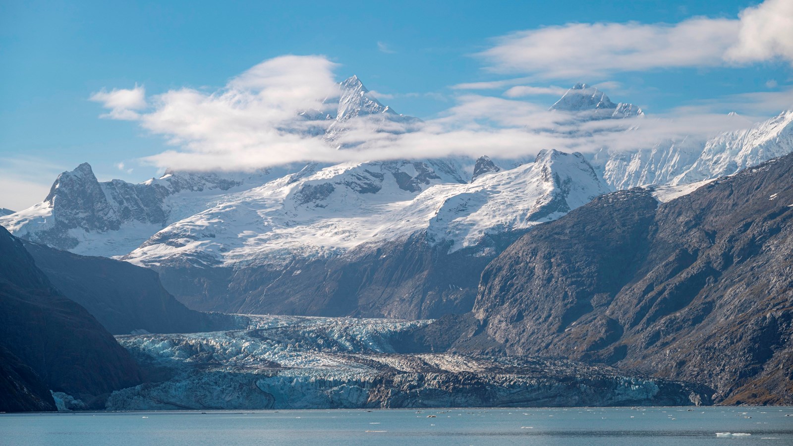 Sparse chunks of ice float in the water in front of Johns Hopkins Glacier on a sunny day.