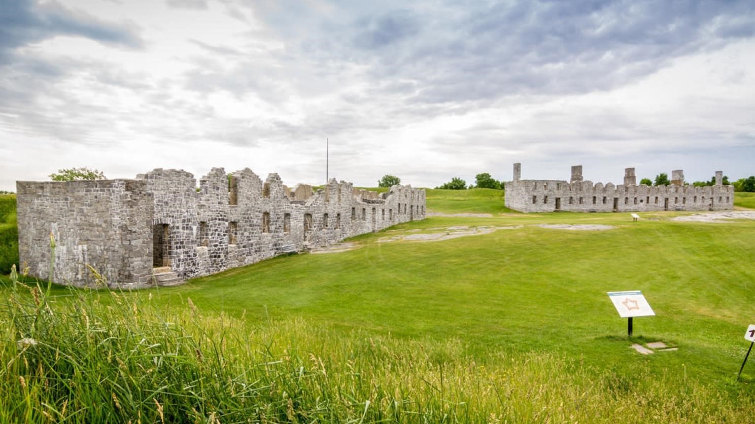 Remains of two massive brick buildings with no roofs left, sitting in the middle of a field.