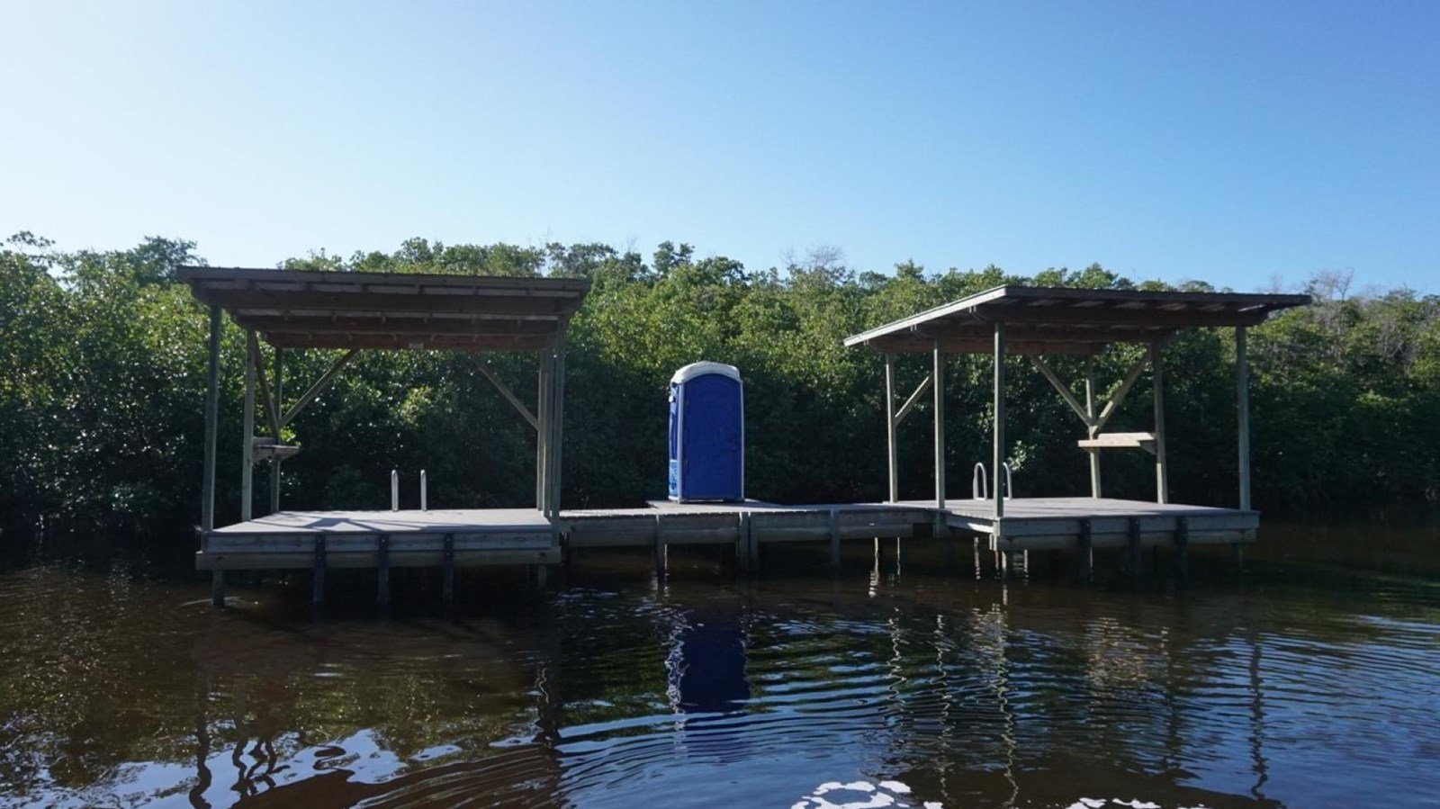 Two roofed, open air platforms sit elevated over the water. A blue vault toilet sits between them