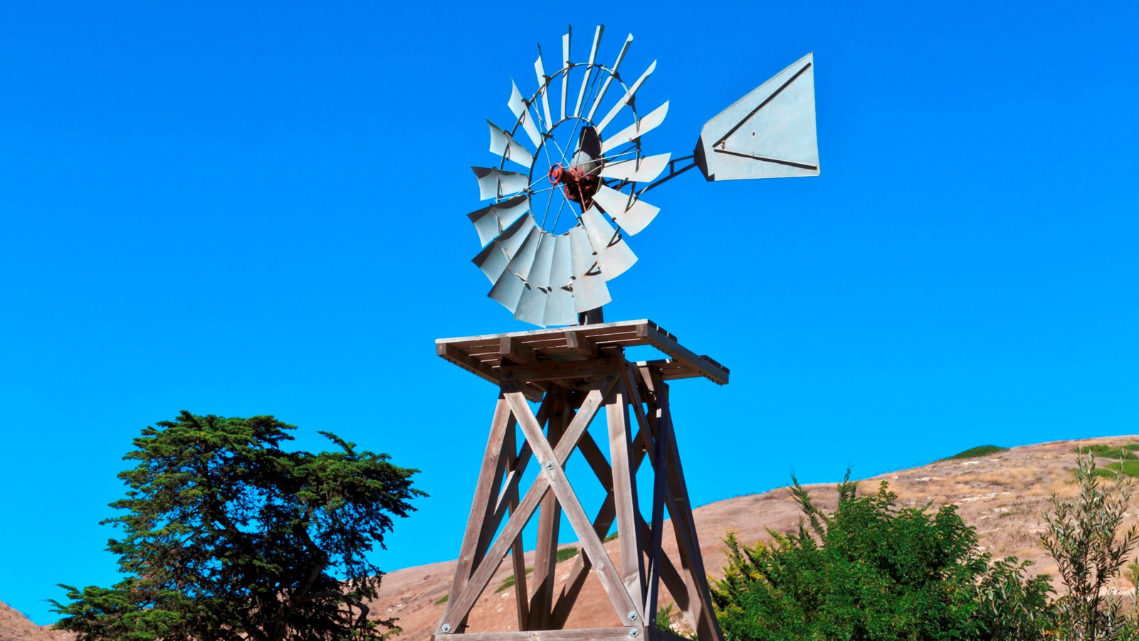 windmill on a wooden scaffold with a circular set of turbine blades like petals on a sunflower.