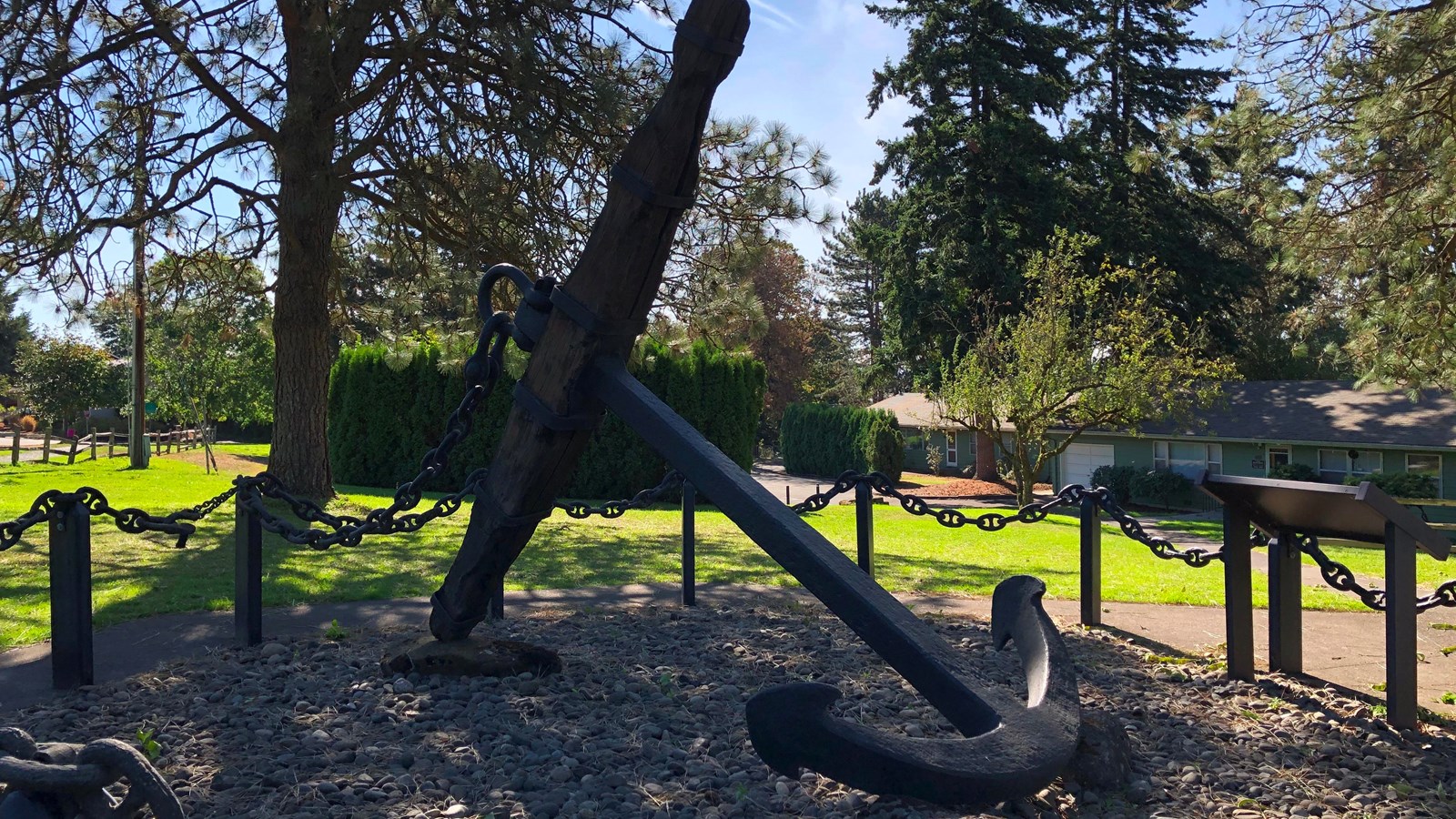 A very large metal and wood anchor surrounded by a chain barrier.
