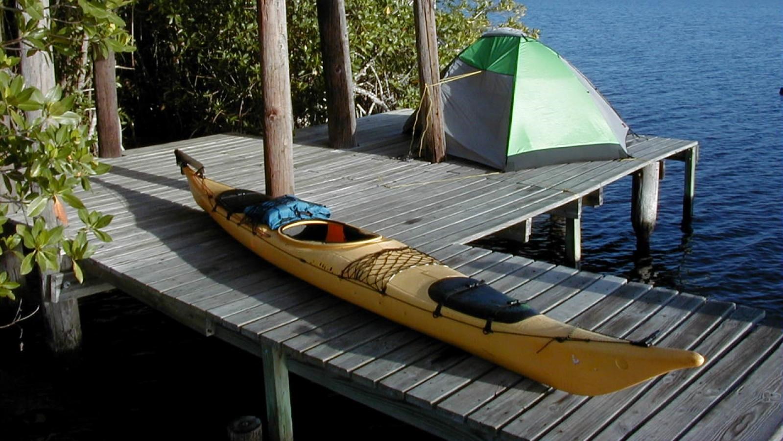 A yellow kayak sits atop a wooden platform above the water. A green tent is behind it