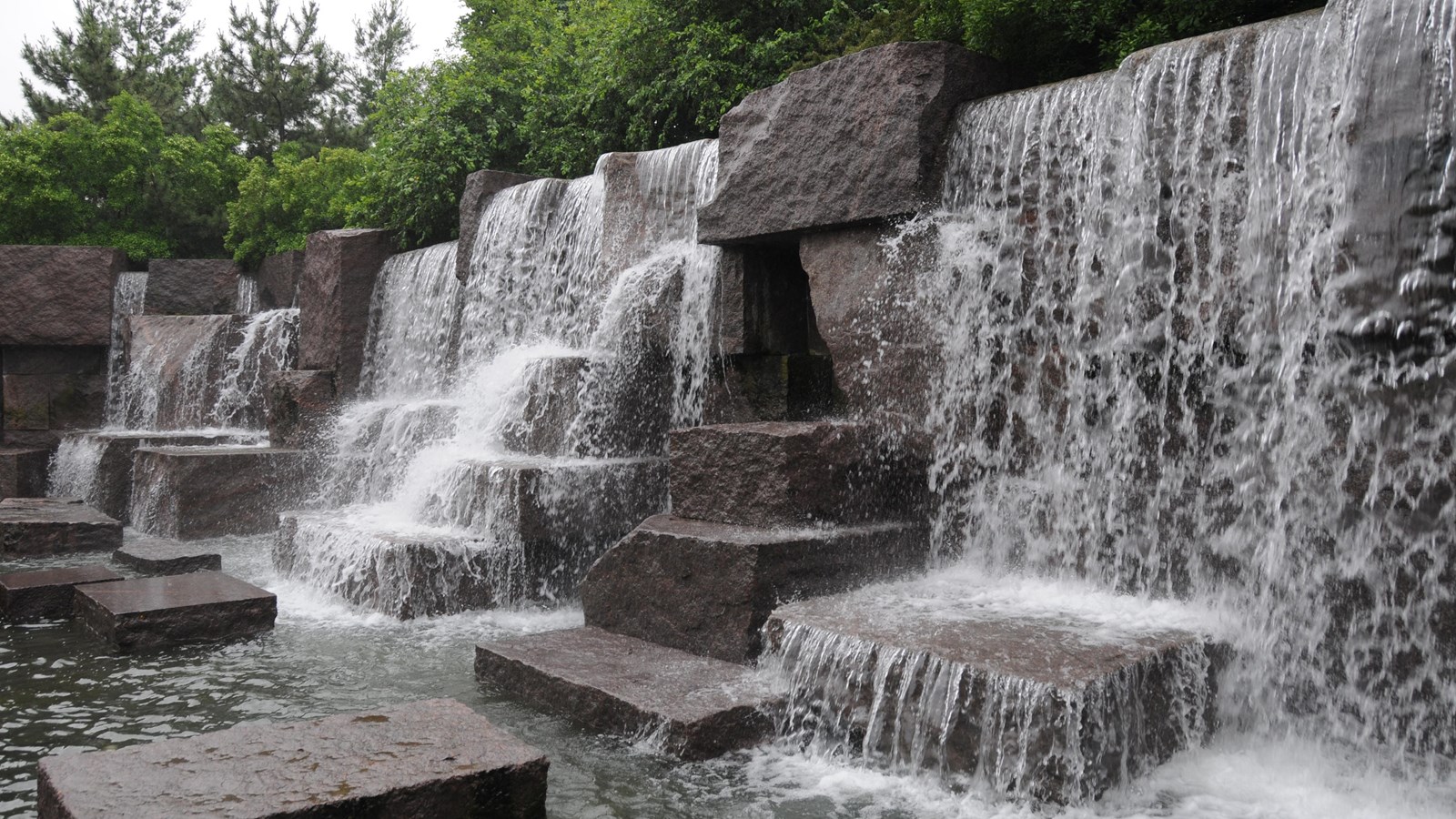 Water is falling down on various stones. Greenery falls over the water fall. 