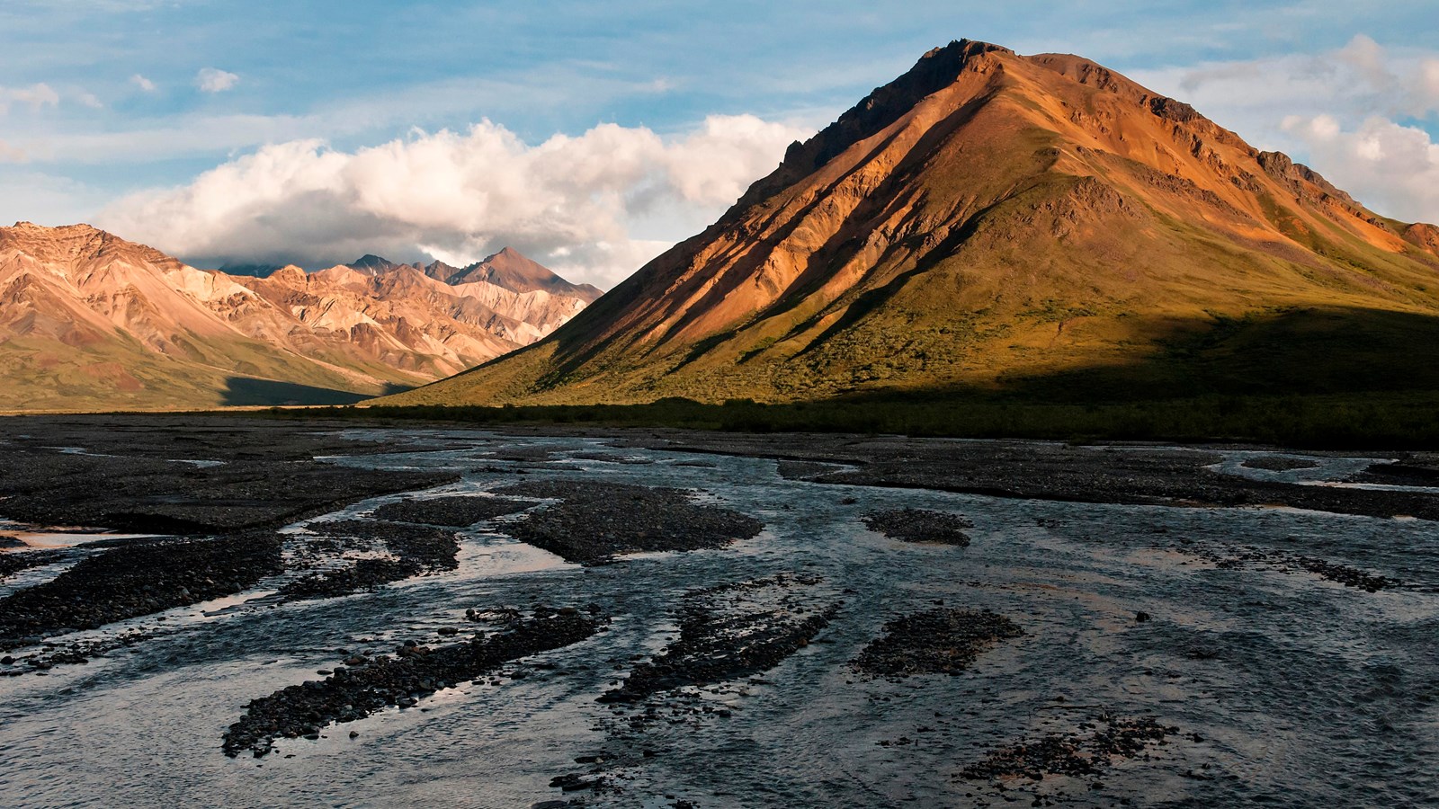 two streams, one blue and one gray, flow together at the foot of a mountain