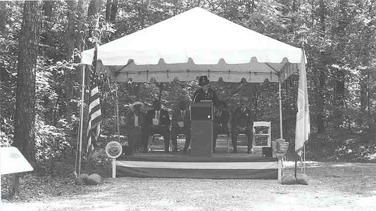 Black and white photo of canopy, covering 4 people with a podium.