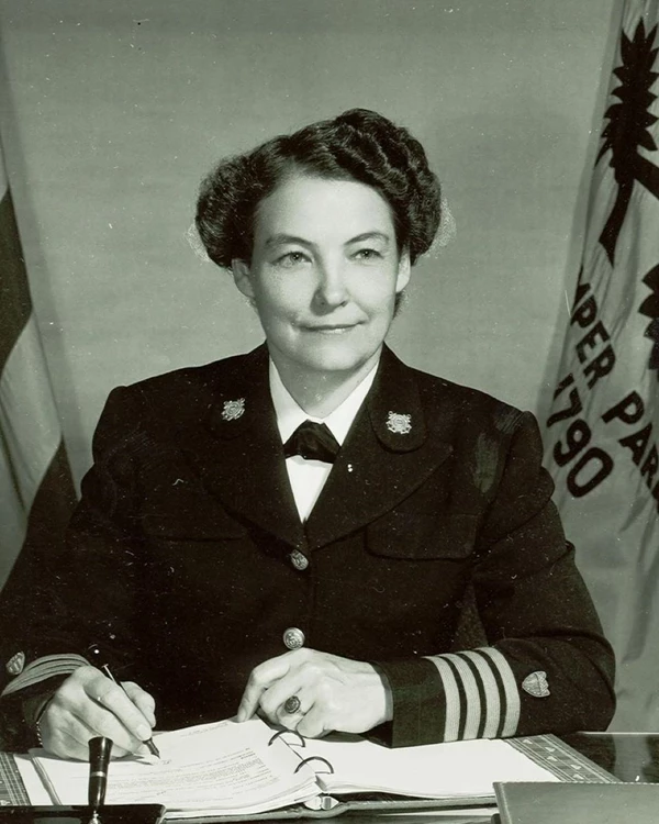 Black and white photo of a white woman with dark hair in a dark military uniform sitting at a desk w