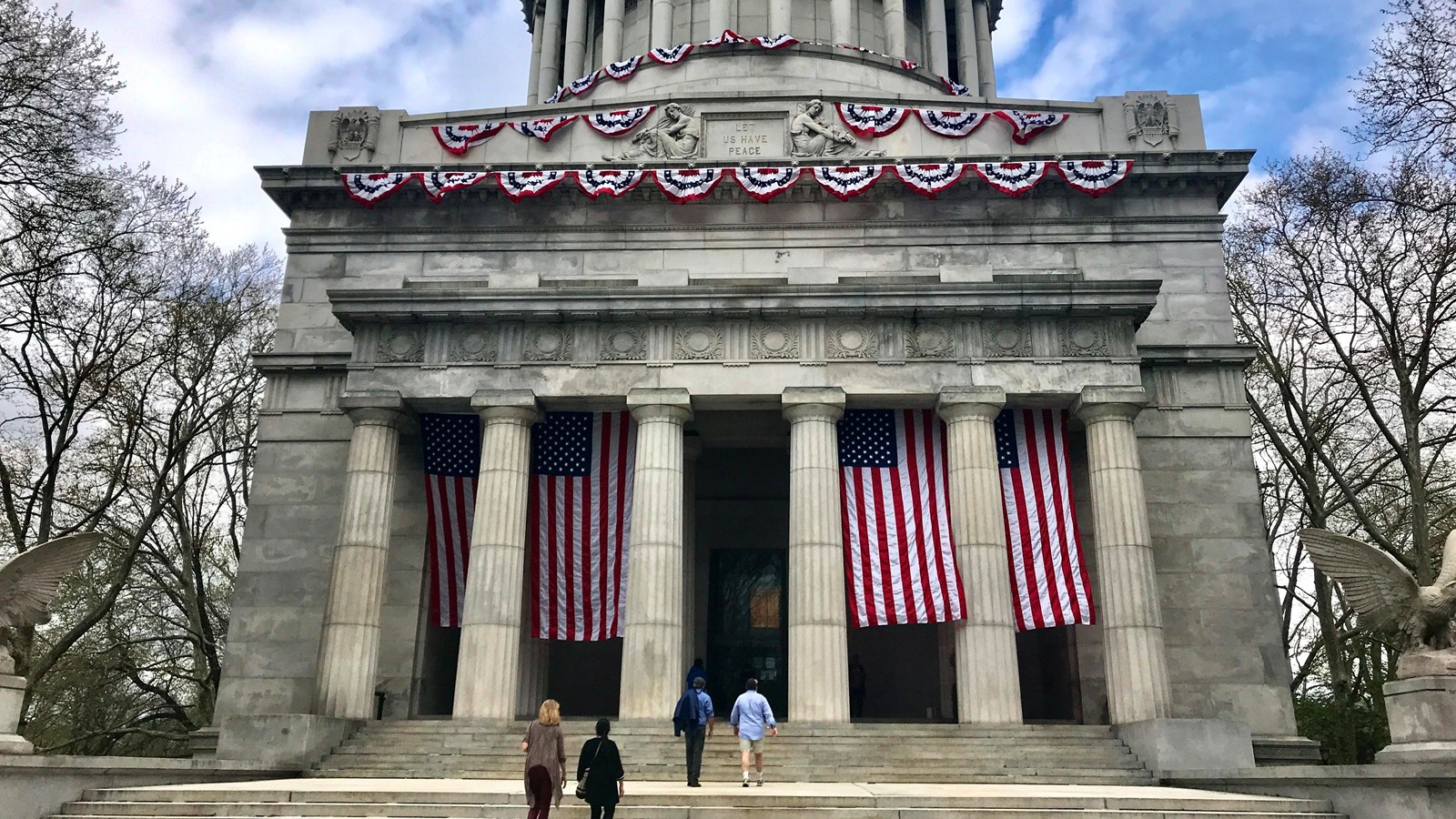 front of tomb with dome, columns, flags and people walking on broad steps