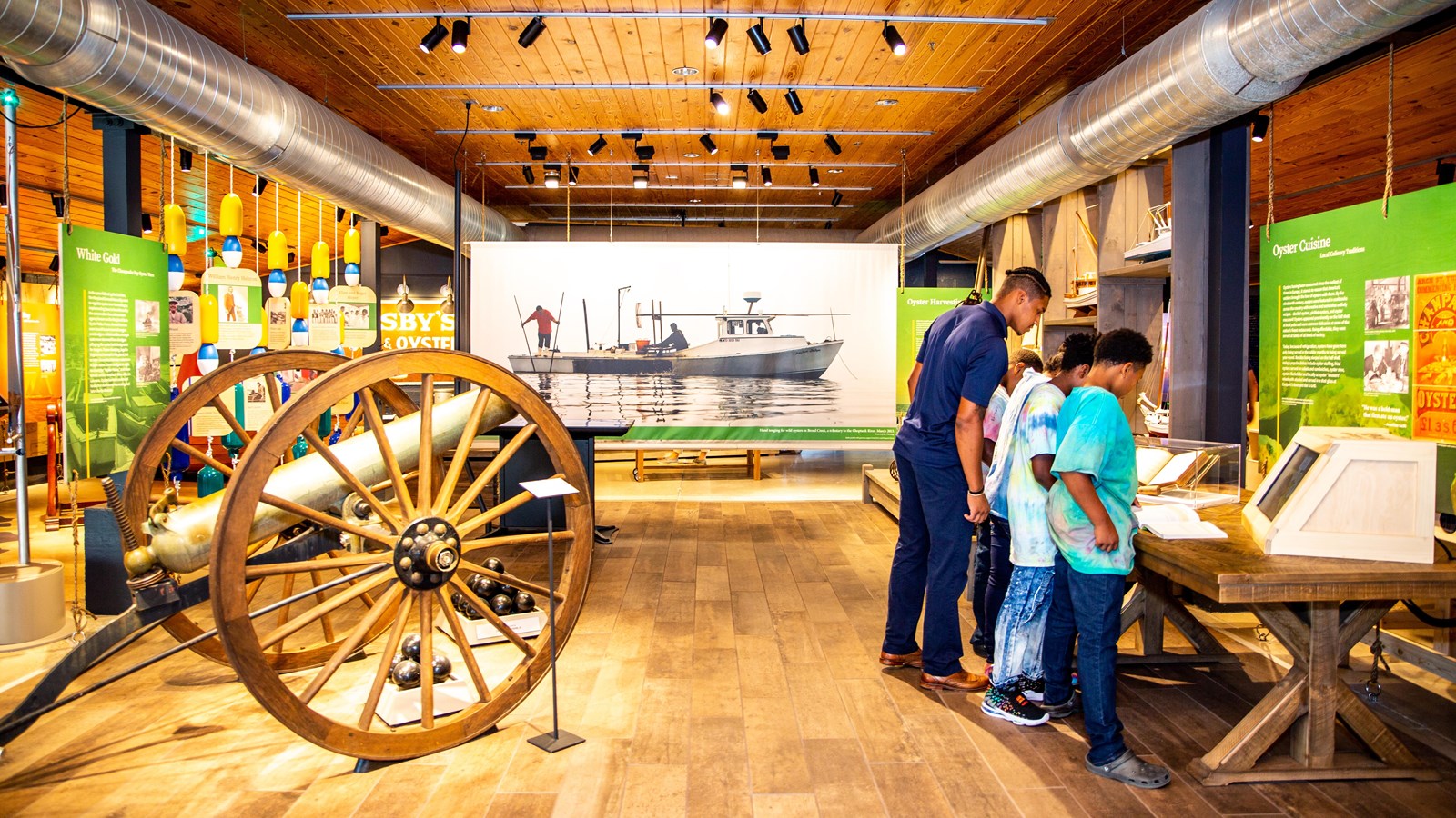 Museum exhibit with a wooden cannon as a man and four children look at a book.