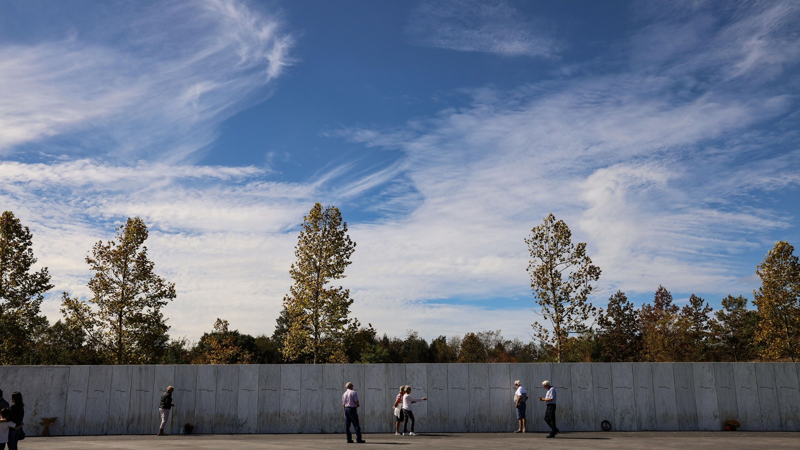 Visitors at Wall of Names with blue sky and clouds in the background.