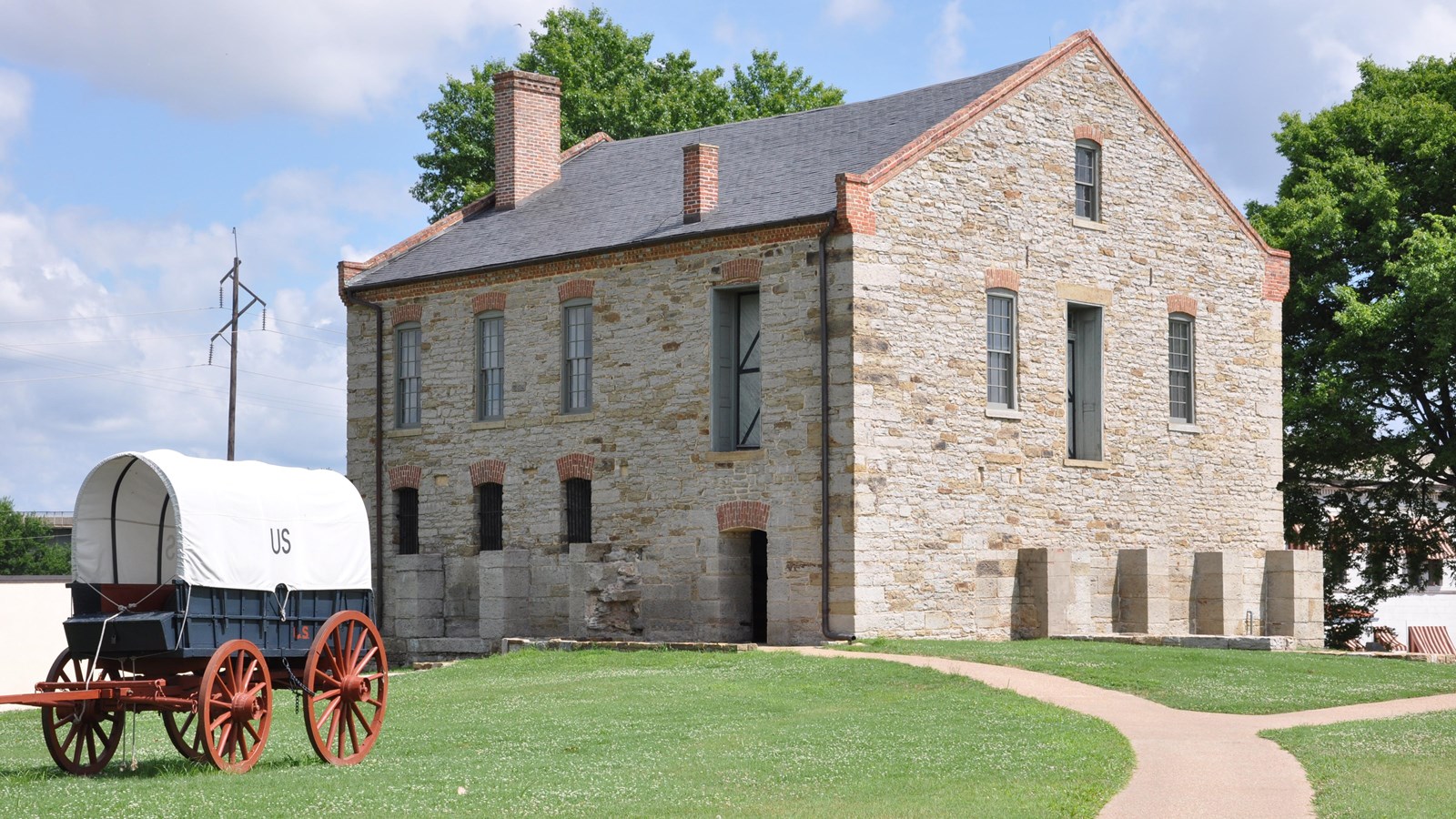 Supply wagon parked in front of two-story light tan stone building with gray slate tile roof.