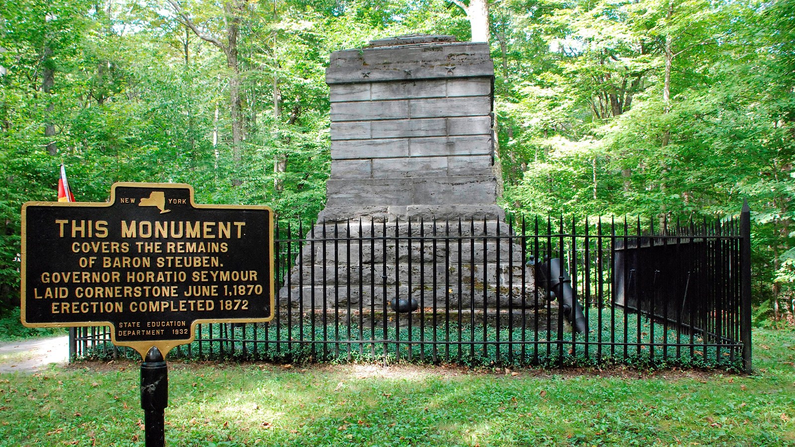 A large block, stone monument behind a rod iron fence.