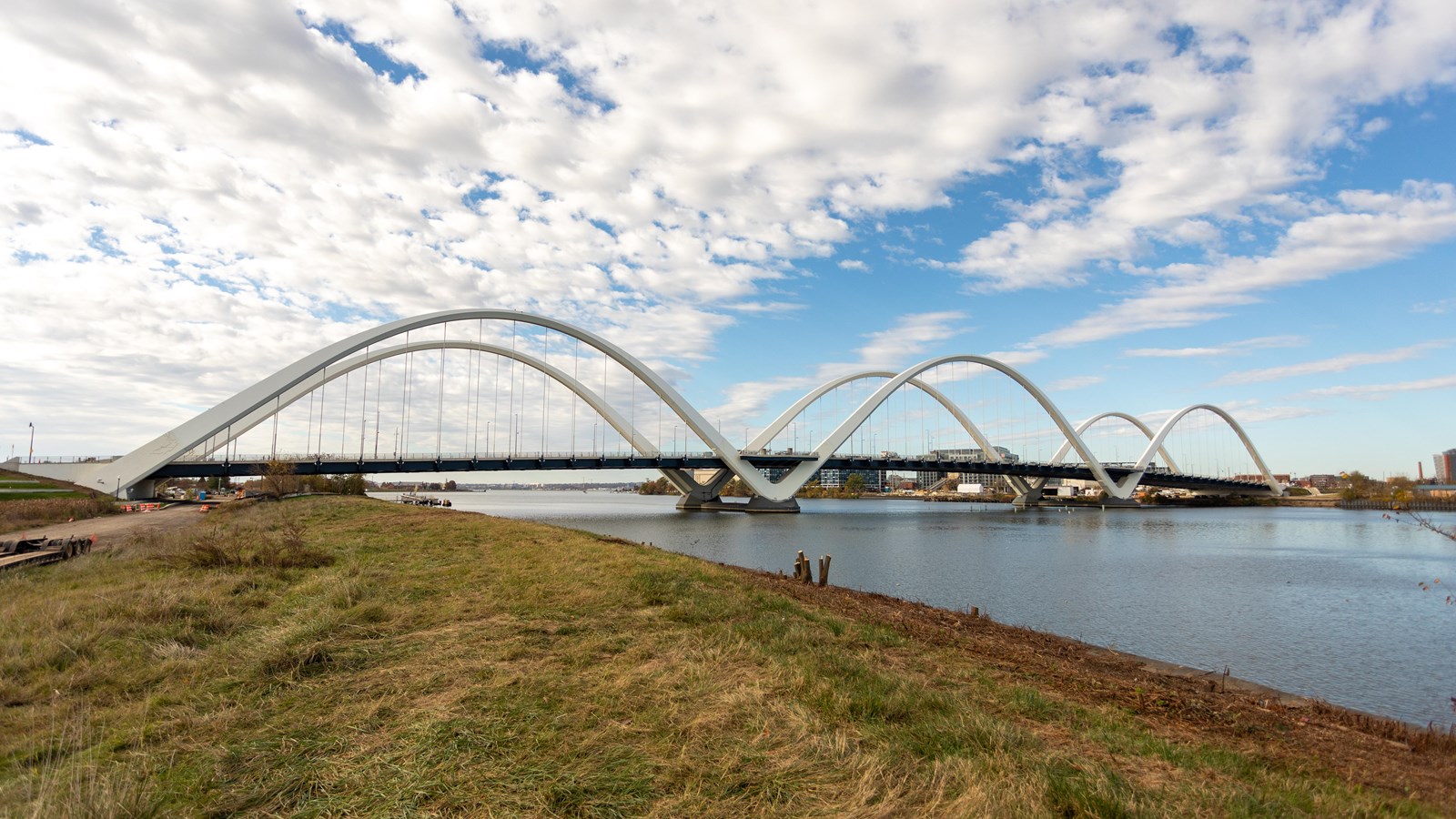 A white bridge has three, half-circular designs on either side. Blue water is stagnant below.