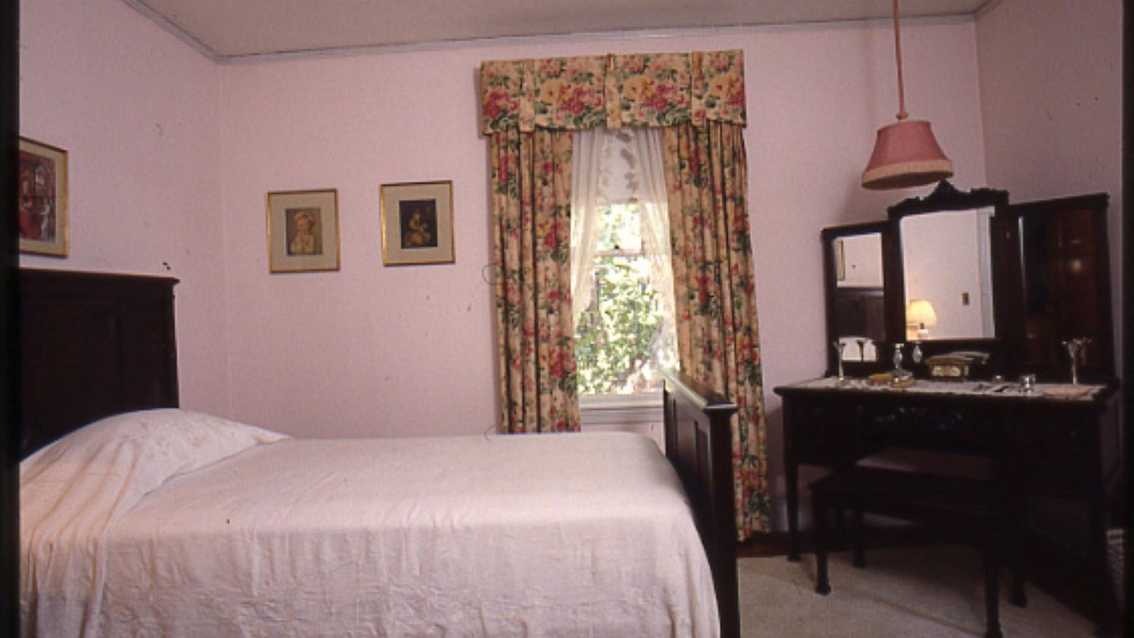 Bedroom with dark wood furniture set, twin bed covered with off-white blanket. Pink and tan floral d