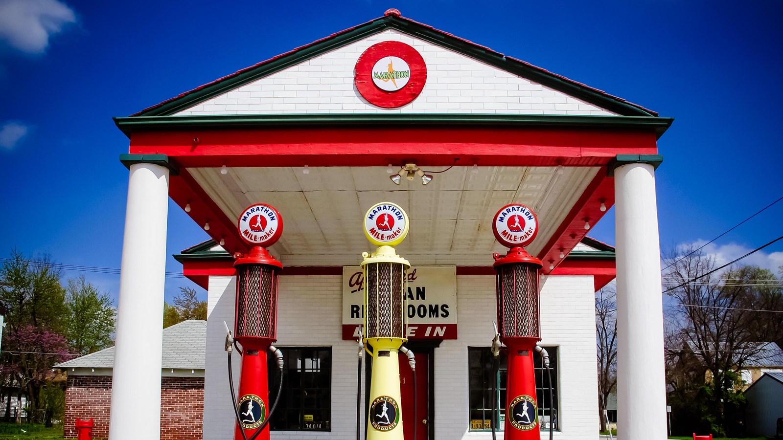 A small white building with a white roof and red and green-black trim. Three gas pumps sit outside.