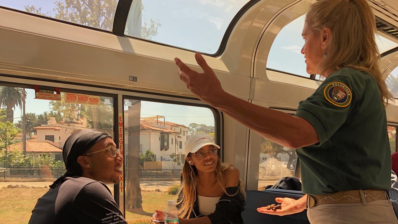 A volunteer is talking to two railroad passengers onboard a train.
