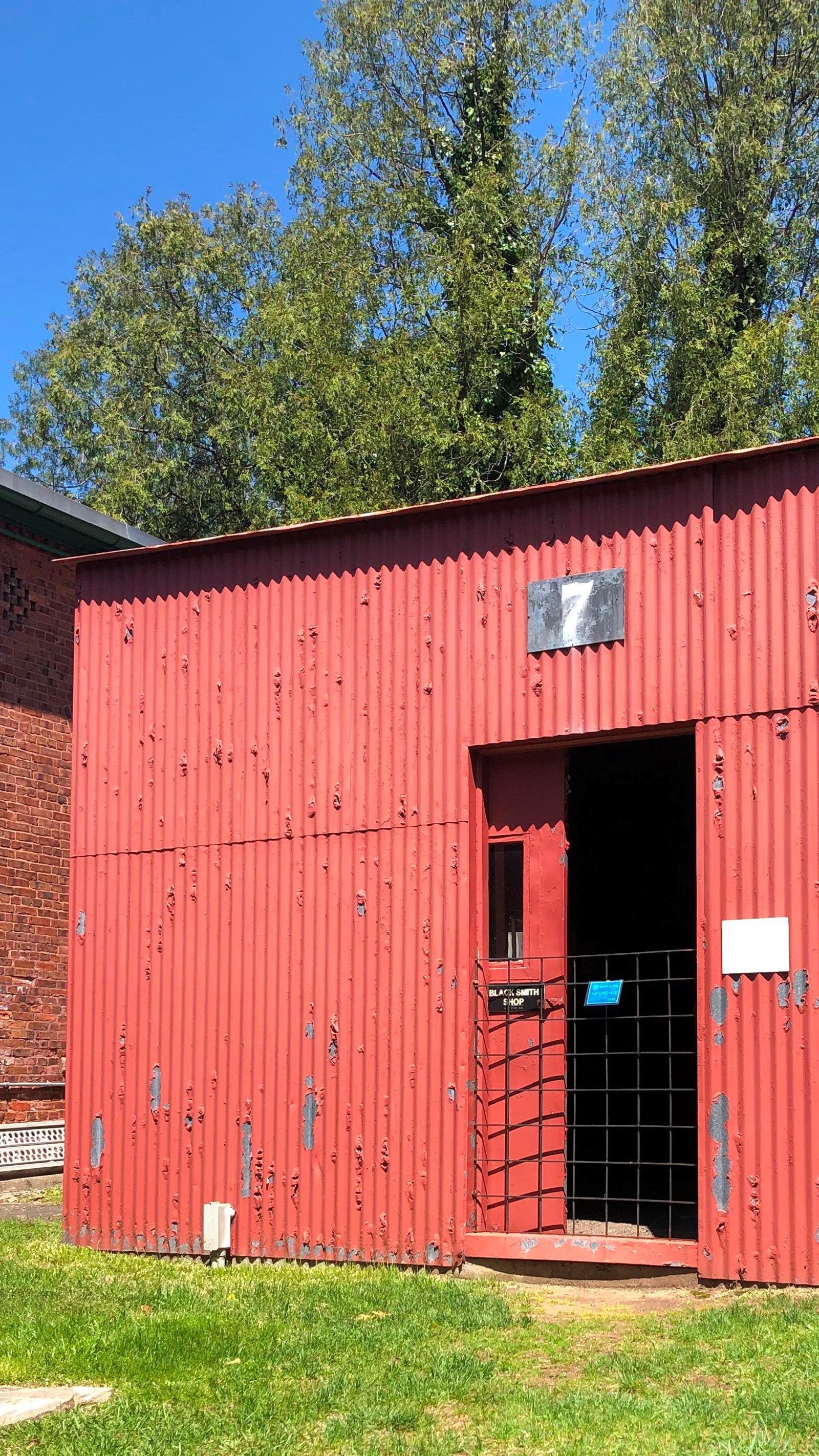 Square corrugated metal building, painted red with half open pocket door. 