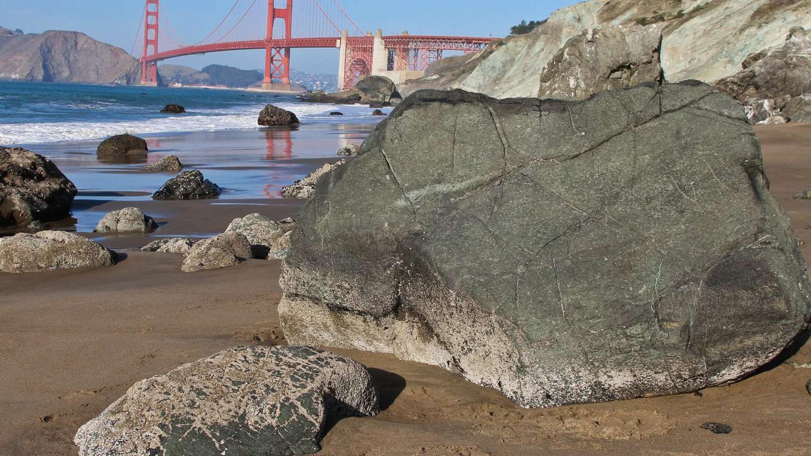 Large serpentinite blocks on Marshall\'s Beach with green and gray cliffs and the Golden Gate Bridge