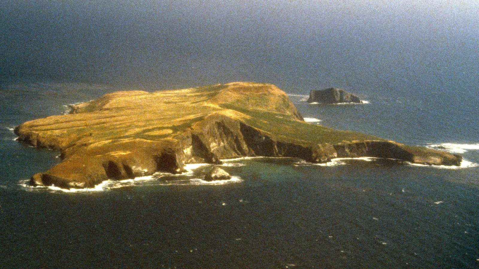 Aerial image of small island with steep cliffs.