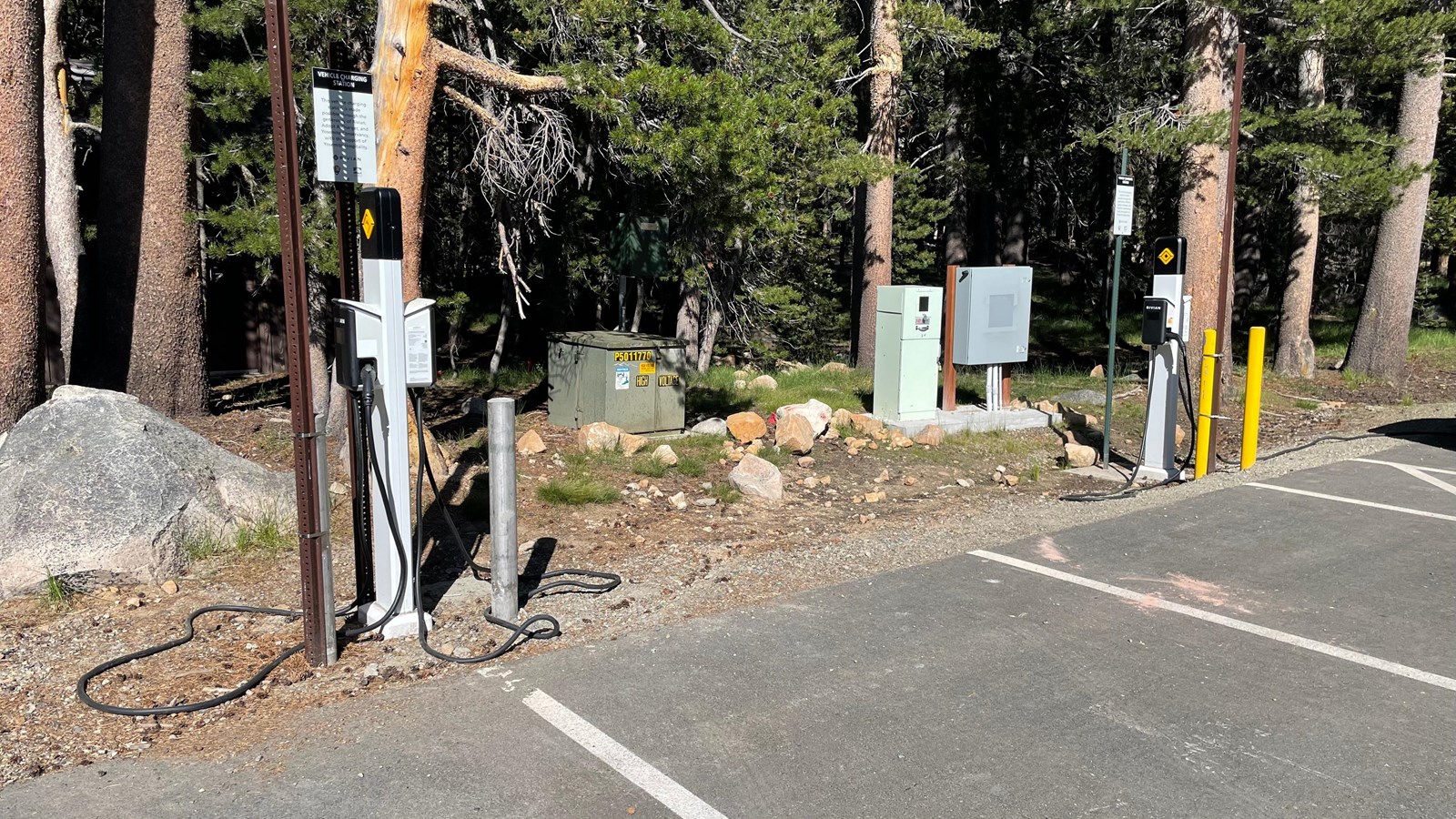 Two electric vehicle charging stations on the edge of a paved parking lot