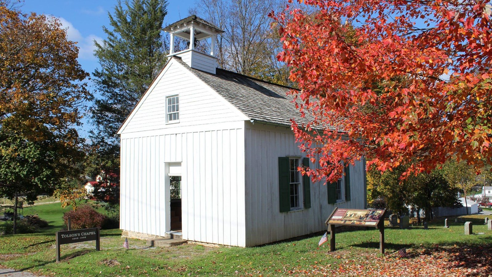 A small white wooden chapel amongst autumn-colored trees.