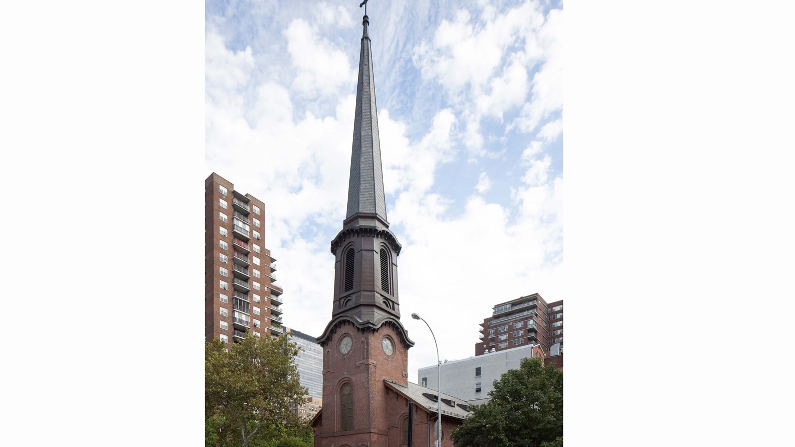 Brownstone church with a large steeple and arched opened for the entrance doors. 