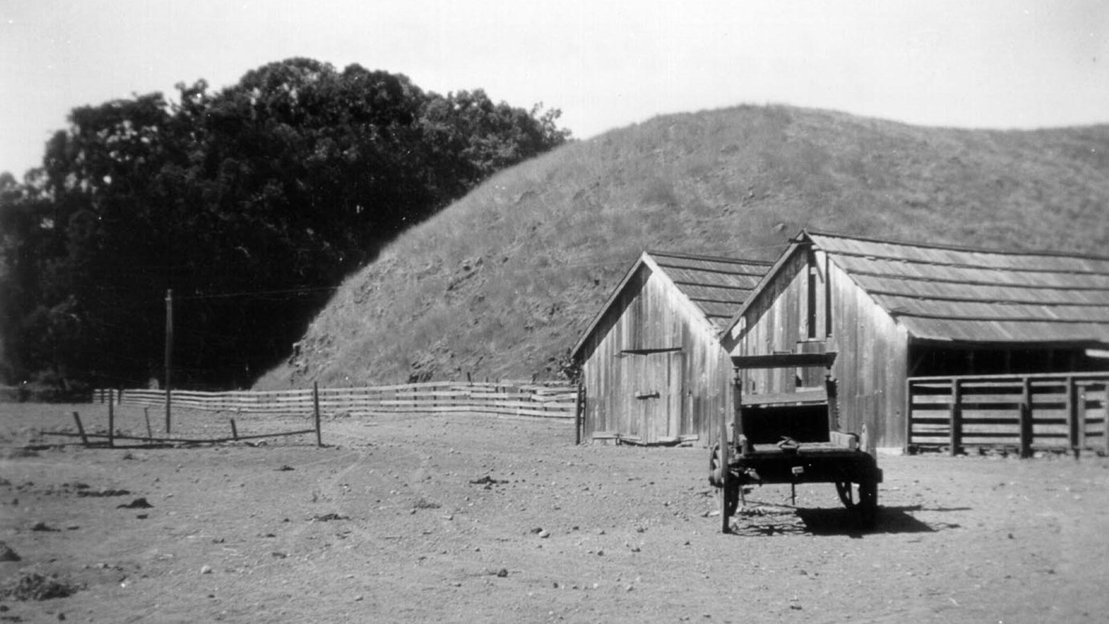 Double gabled barn with dirt road in front and old vehicle.