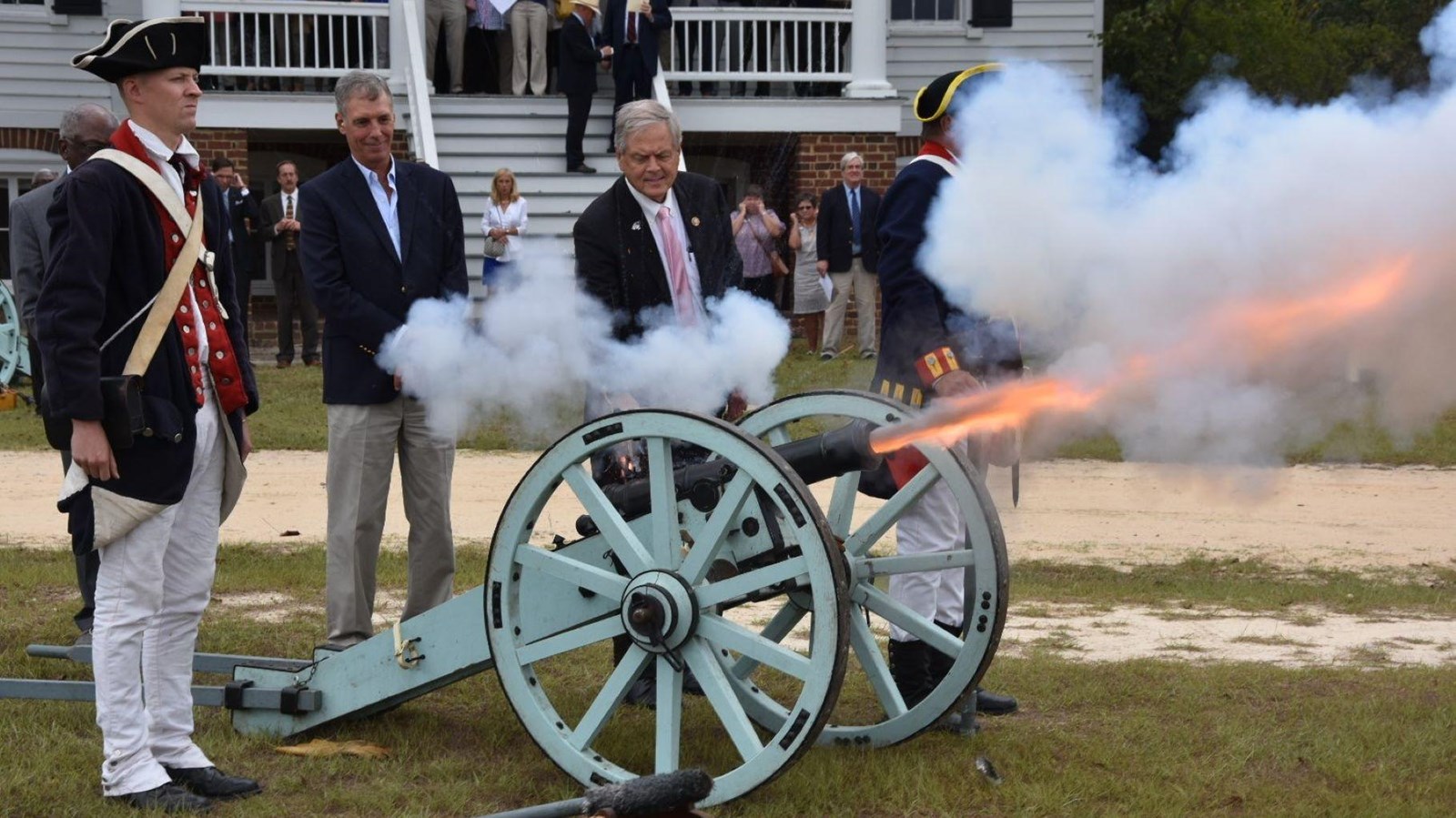 Two white man shoot antique canon with man dressed in Revolutionary War military uniform