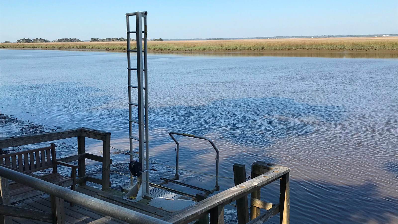 Mechanical kayak lift and wooden platform with river and salt marsh in background.